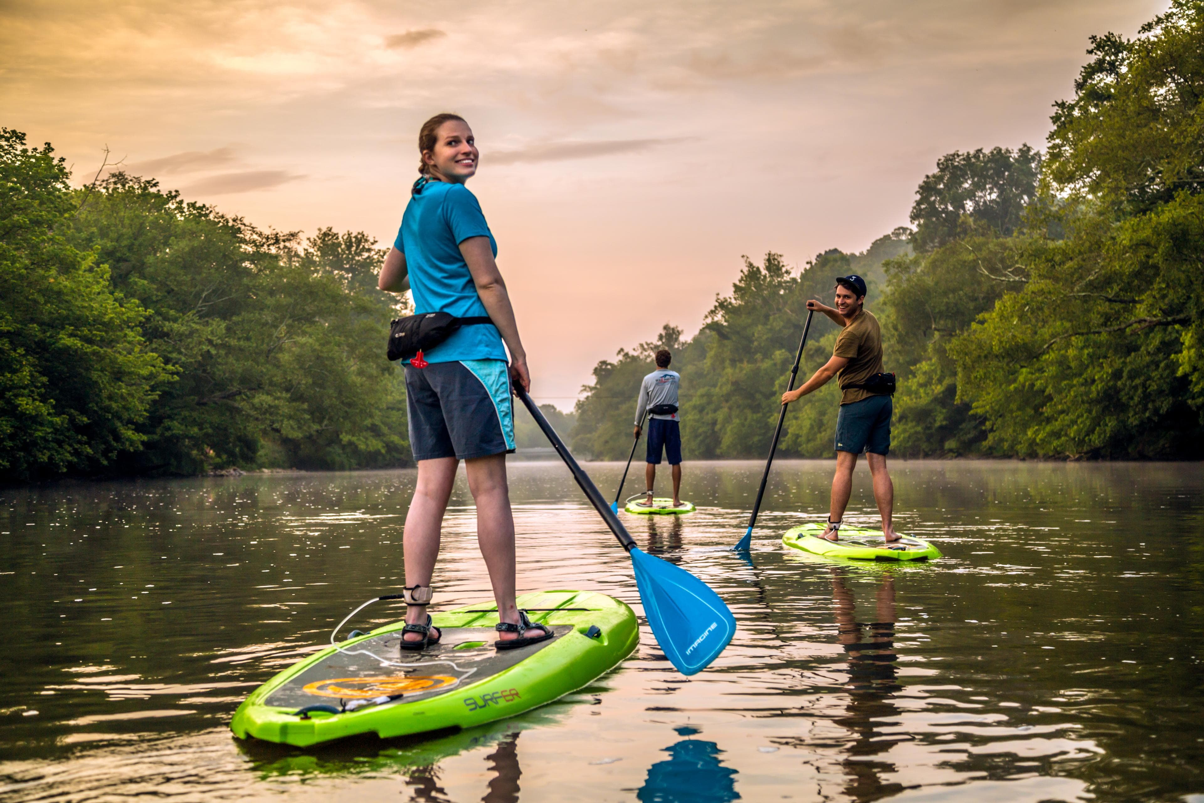 Adventures on the Third Oldest River in the World Three people paddle down an Asheville waterway at sunset