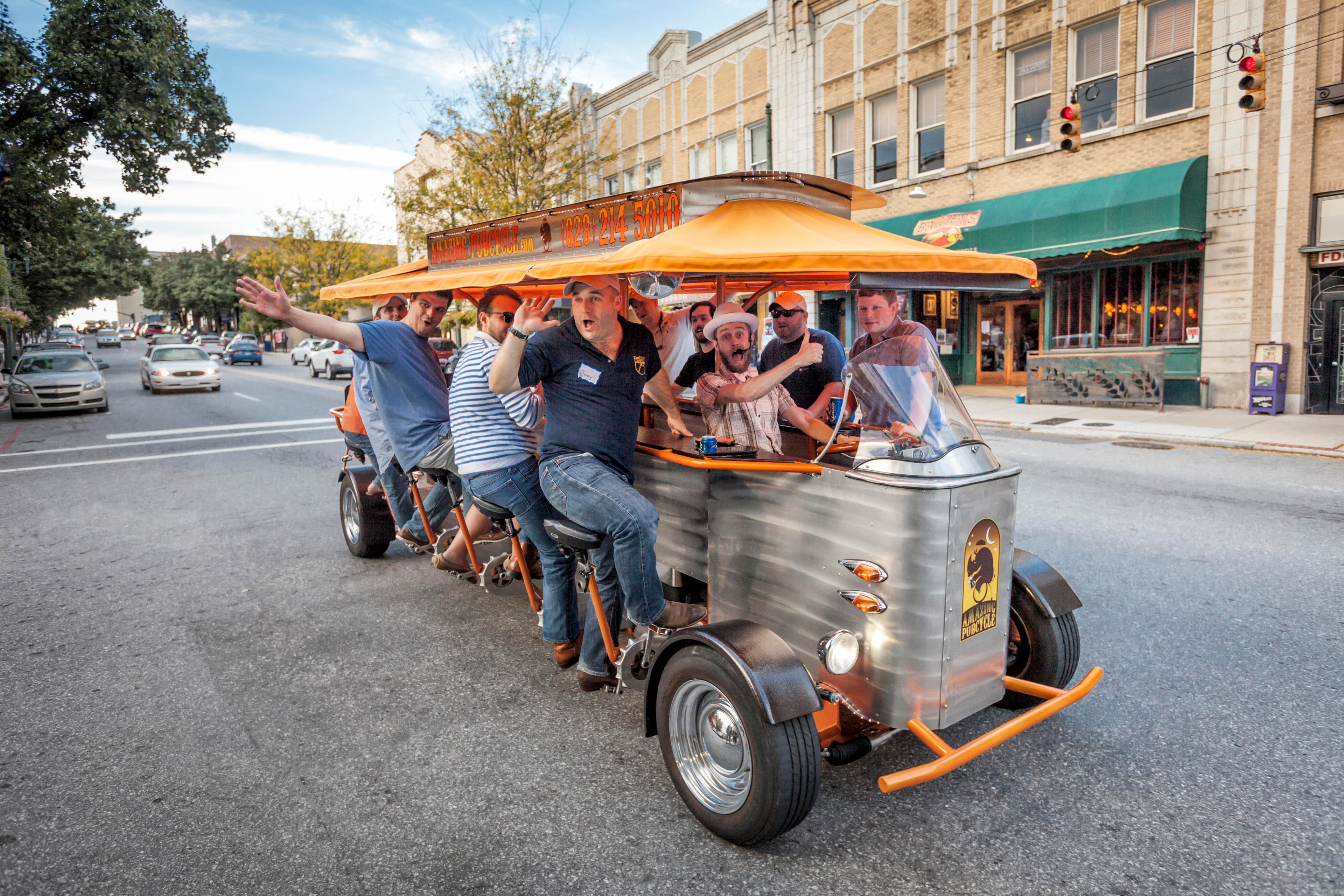 Asheville Beer Tours, Tastings & Tips A group of people laugh as they pedal on a moving bar on a beer tour in Asheville