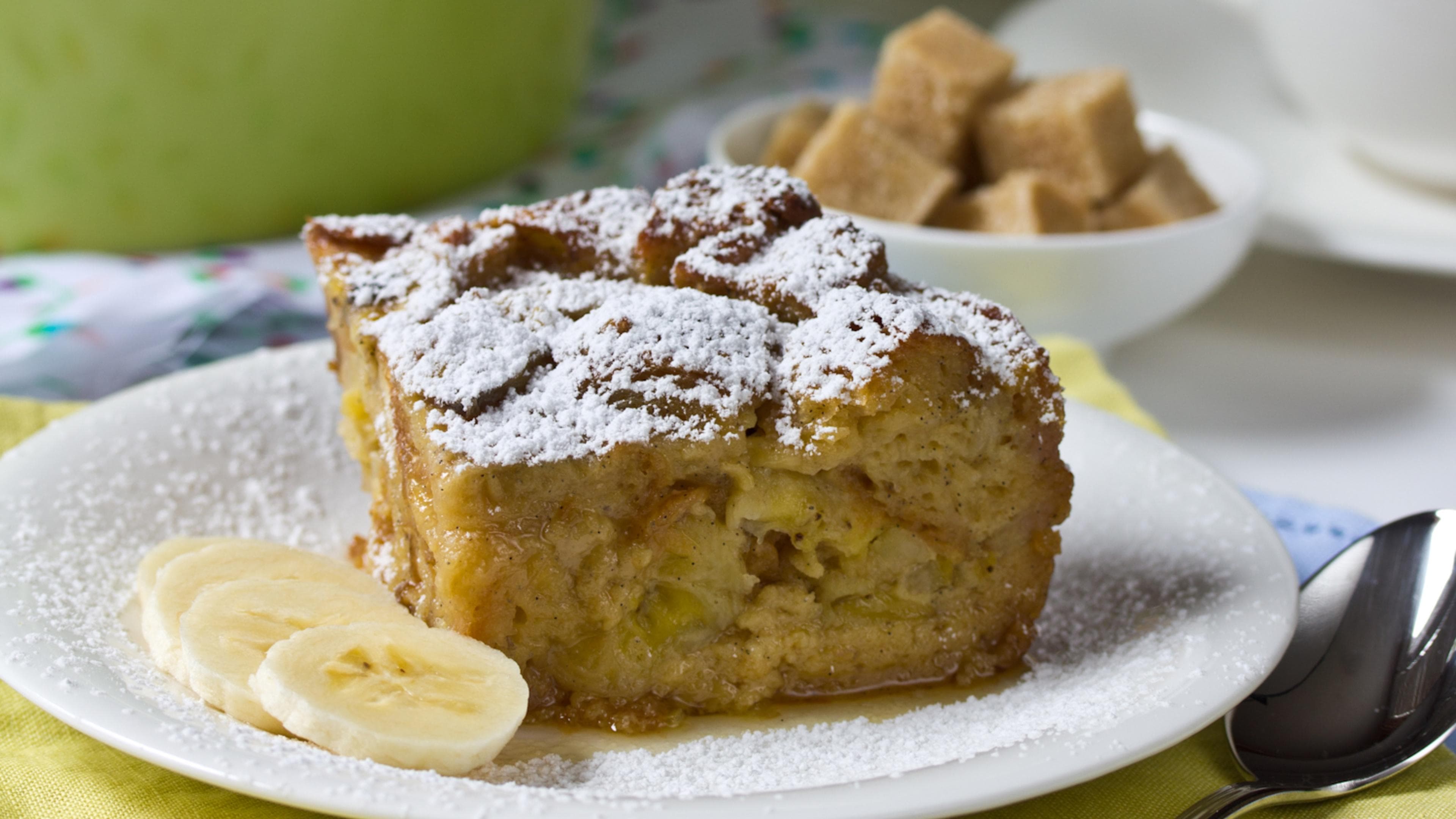 a square of banana bread pudding sprinkled with powdered sugar and sliced bananas on the side a square of banana bread pudding sprinkled with powdered sugar and sliced bananas on the side
