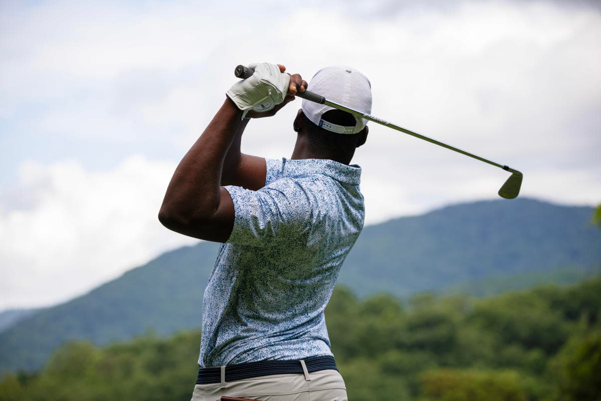 Outside image of a person at the peak of a golf swing with a mountain range in the background. Outside image of a person at the peak of a golf swing with a mountain range in the background.