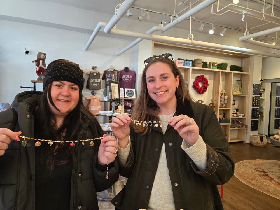 2 women holding finished necklaces made at DIY charm bar 2 women holding finished necklaces made at DIY charm bar