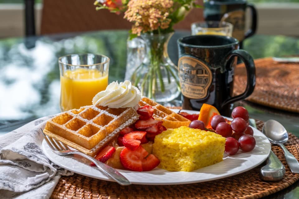 A breakfast plate of Belgian waffles with fresh strawberries, eggs, and fruit, served at Pinecrest Bed and Breakfast with orange juice and a Pinecrest coffee mug A breakfast plate of Belgian waffles with fresh strawberries, eggs, and fruit, served at Pinecrest Bed and Breakfast with orange juice and a Pinecrest coffee mug